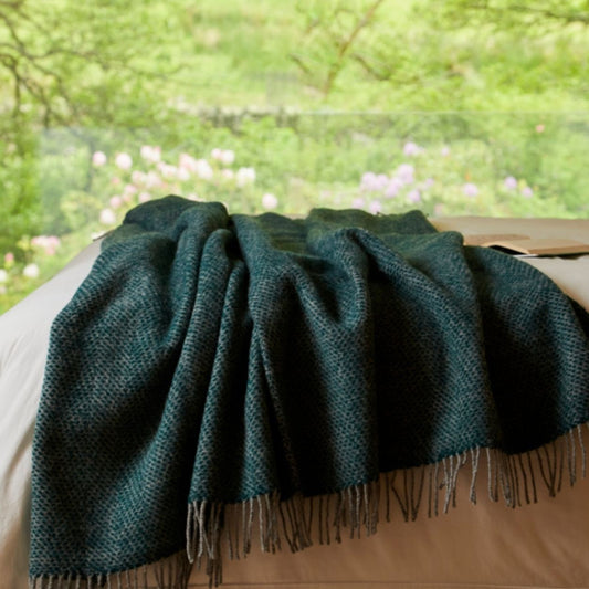 Green blanket with fringes draped over a surface with a blurred natural background