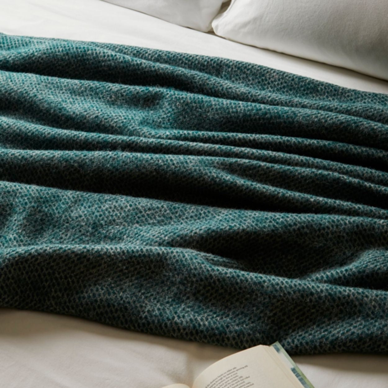 Green textured blanket draped over a bed with an open book underneath.