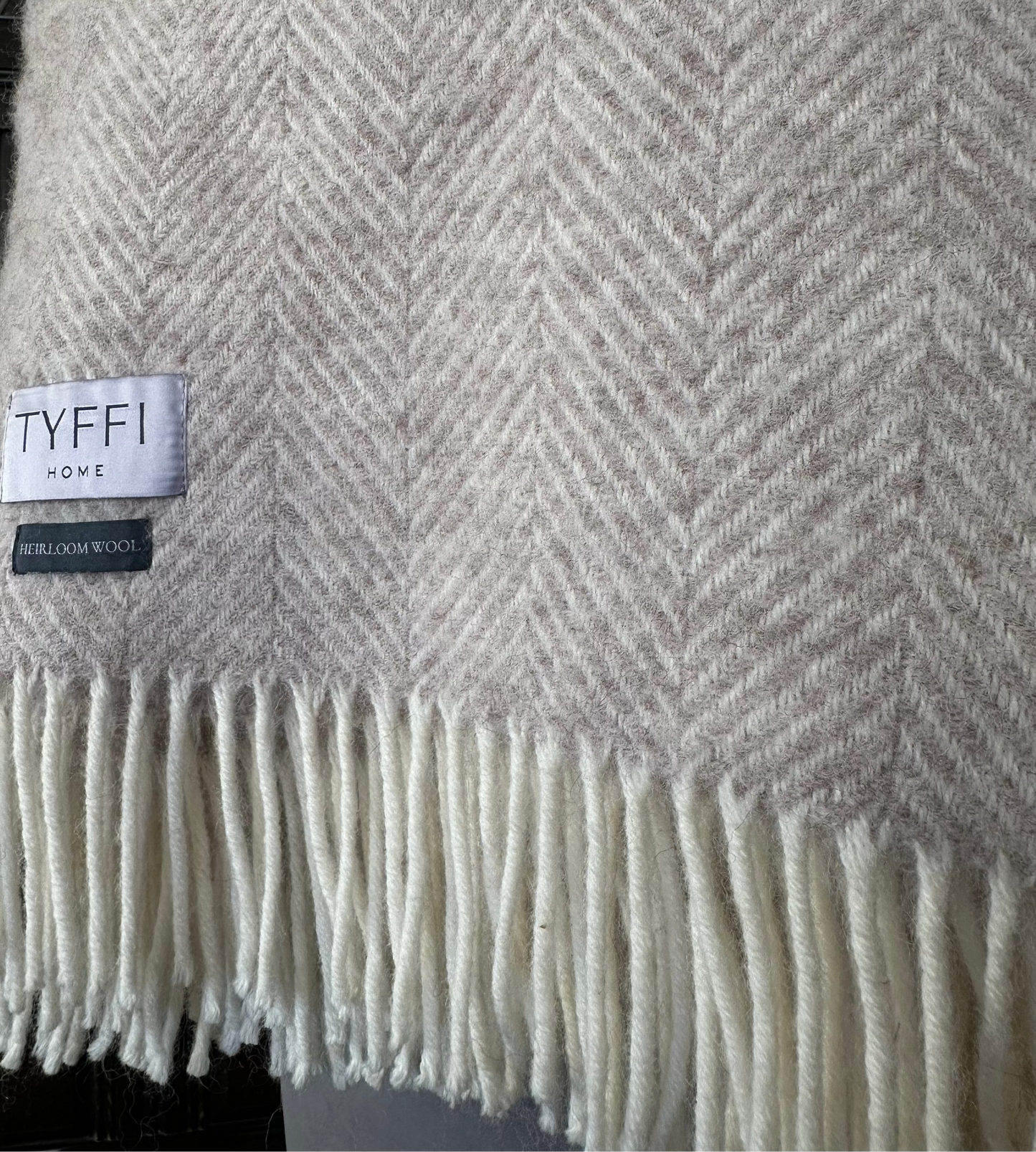 Close-up of a herringbone-patterned blanket with a brand label on a dark background
