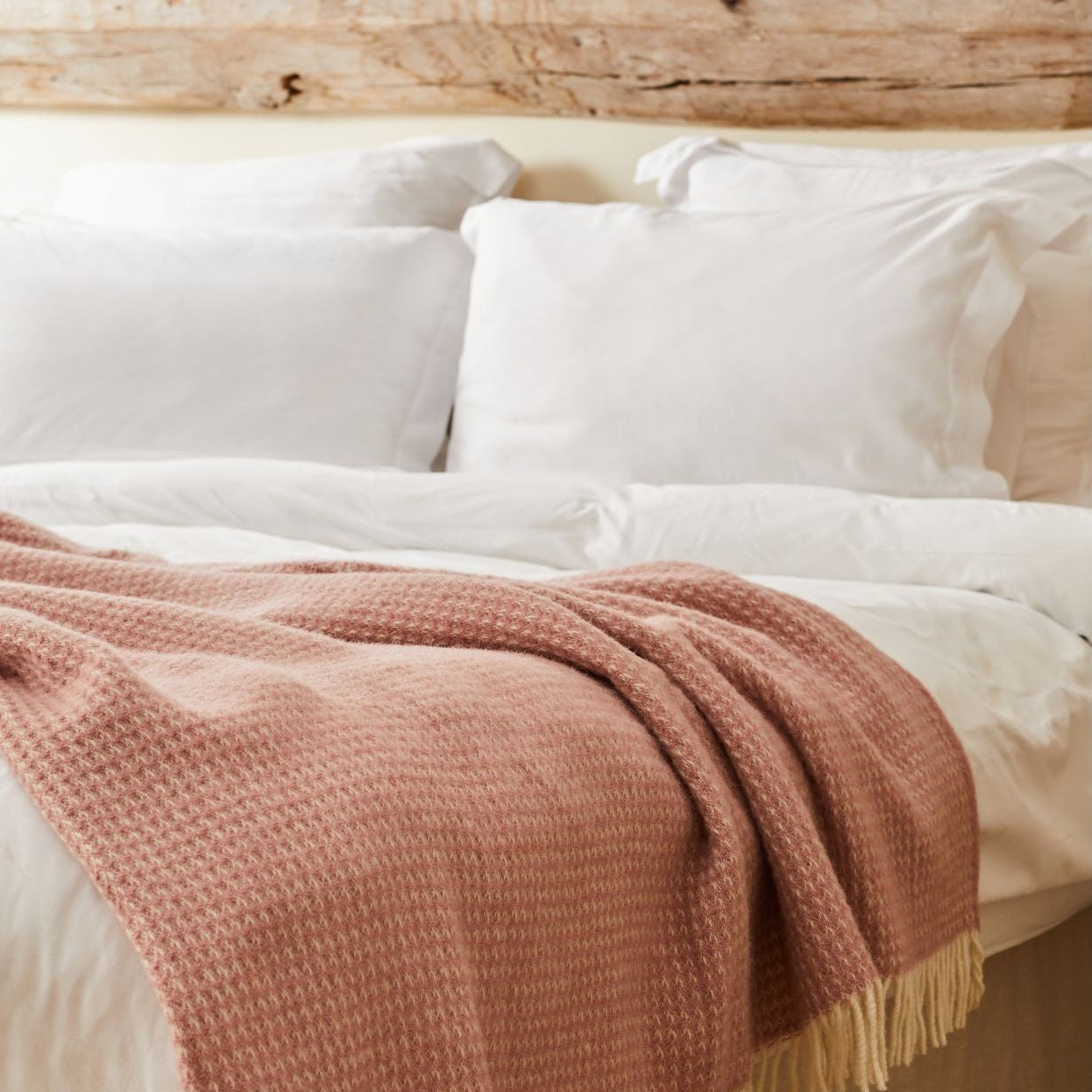 Bed with white pillows and a pink blanket against a wooden headboard.