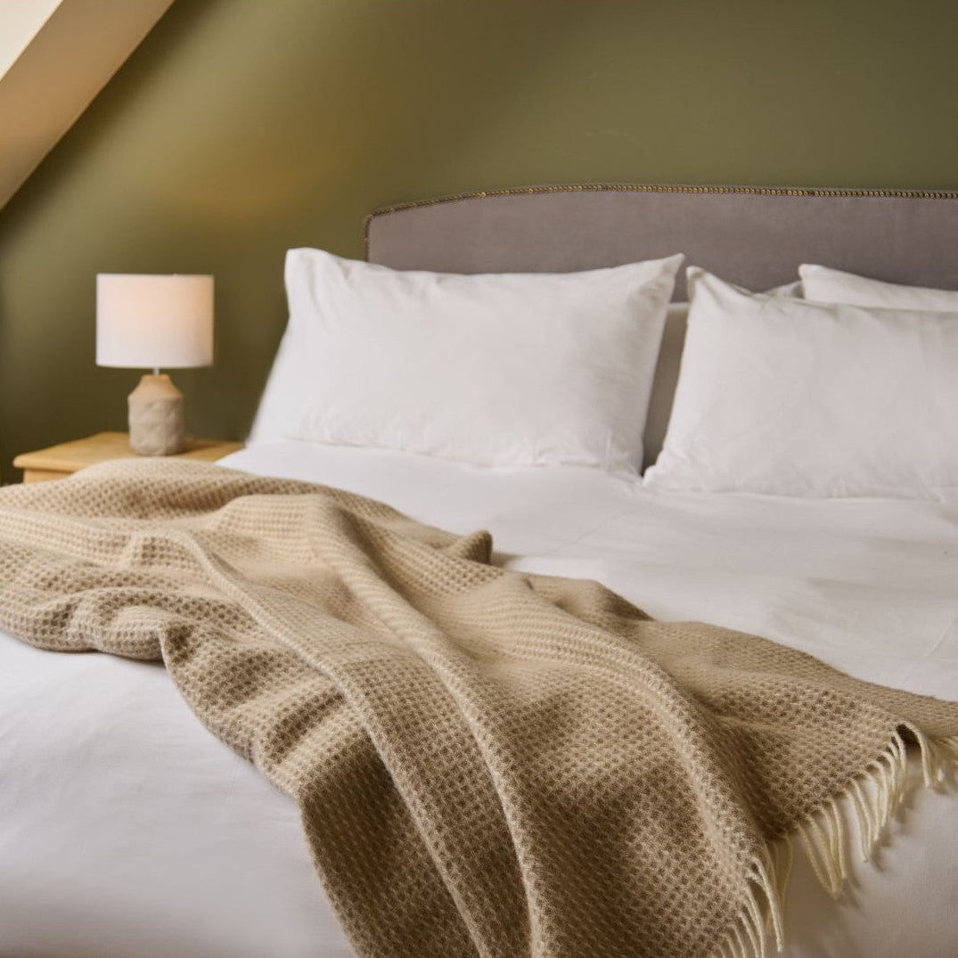 Bed with beige blanket and white pillows in a bedroom setting