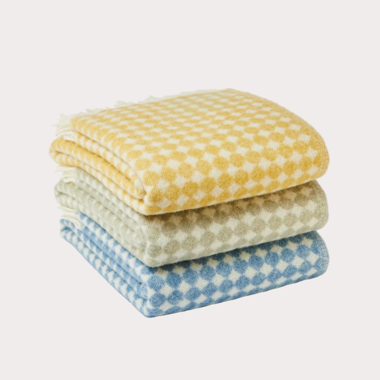Stack of three patterned blankets in yellow, white, and blue on a white background