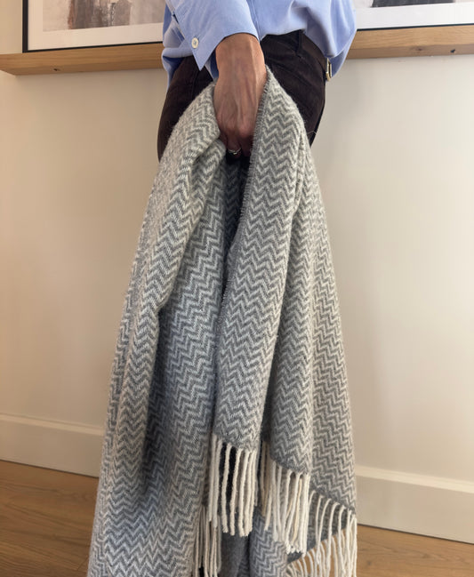 Person holding a gray and white patterned blanket indoors.